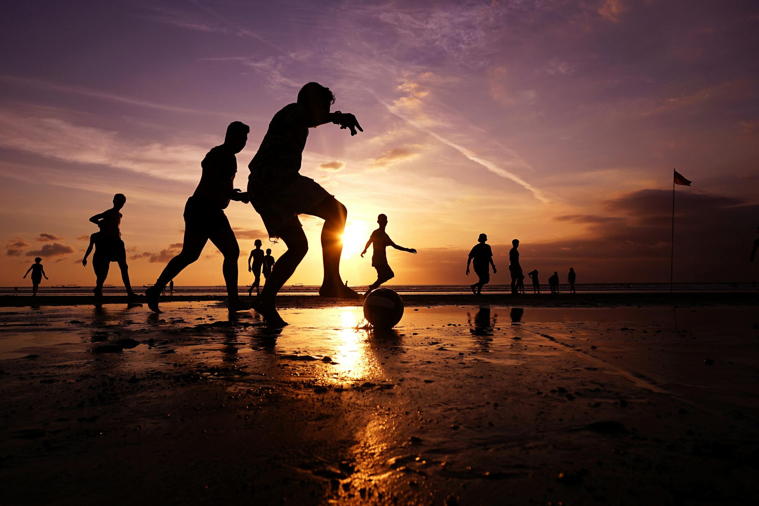 Silhouetted players enjoy a beach football game during a stunning Bali sunset.
